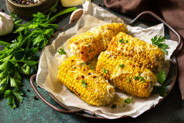 Summer vegan dinner or snacks. Grilled corn with garlic butter, served with cheese on a dark stone table top.
