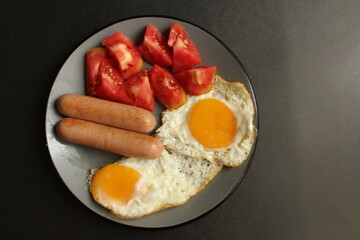 food Breakfast protein fried eggs fried eggs sausage and salad vegetables red tomatoes are on a gray plate on a black background with a copy space