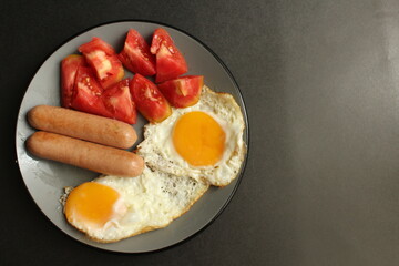 traditional English European Breakfast eggs sausage and salad vegetables red tomatoes on a gray plate on a black background close up side view
