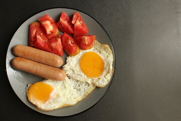 traditional English European Breakfast eggs sausage and salad vegetables red tomatoes on a gray plate on a black background close up side view