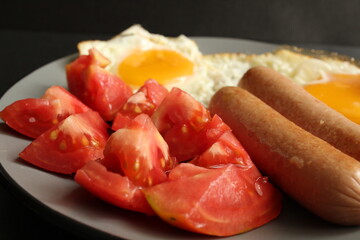 traditional English European Breakfast eggs sausage and salad vegetables red tomatoes on a gray plate on a black background close up side view