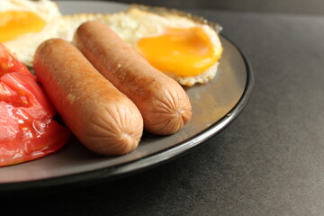traditional English European Breakfast eggs sausage and salad vegetables red tomatoes on a gray plate on a black background close up side view