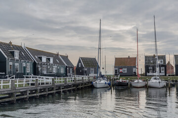 Fototapeta na wymiar Small house with sailing boats moored on a small pier in the harbor with calm water, cloudy sunset with a gray sky in Volendam, the Netherlands Holland