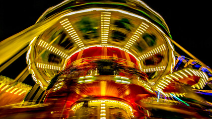 Close-up of a running carousel in high speed rotating motion, illuminated with bright lights of different colors, red, yellow, white and blue with a black blurred background