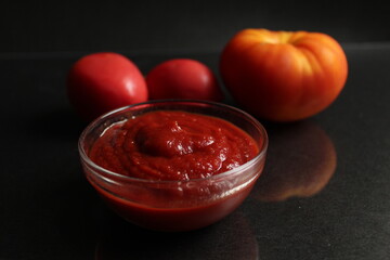 a glass saucepan with red tomato vegetable sauce stands on a black background in the background next to vegetables tomatoes red orange and onions in a yellow husk with copy space