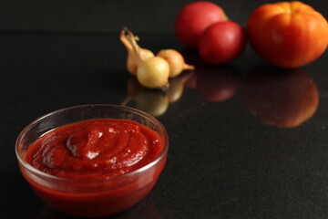 a glass saucepan with red tomato vegetable sauce stands on a black background in the background next to vegetables tomatoes red orange and onions in a yellow husk with Kopi space