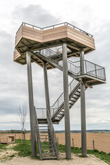 Fototapeta na wymiar Metal staircase of the Mesch watchtower between farmland with its support posts and the upper platform with a wooden railing, overcast day with gray sky in Eijsden, South Limburg in the Netherlands