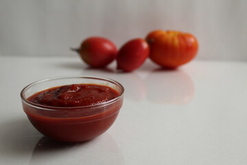 red tomato sauce ketchup in a glass salad bowl saucepan on a white background are vegetables in the background red tomatoes