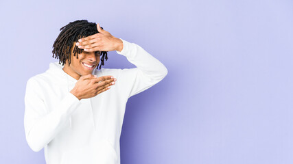 Young african american rasta man blink at the camera through fingers, embarrassed covering face.