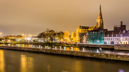 Obraz premium Night view of the river Maas (Meuse) with beautiful reflections of multicolored lights on a quiet December night in Maastricht, South Limburg in the Netherlands Holland