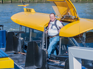 Smiling man in casual clothes disembarking from a taxi boat at a pier on the banks of the Maas river in the city of Rotterdam, sunny day in the Netherlands Holland