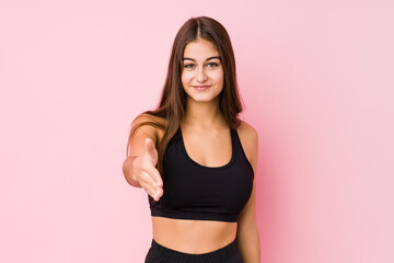 Young caucasian fitness woman doing sport isolated stretching hand at camera in greeting gesture.
