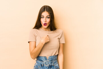 Young caucasian woman isolated en beige background surprised pointing with finger, smiling broadly.