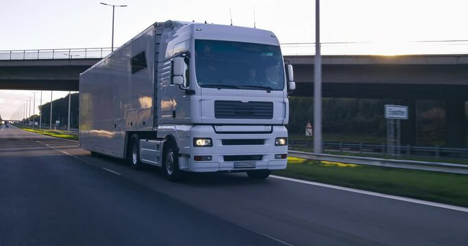 Cargo truck with cargo trailer driving on a highway. White Truck delivers goods in early hours of the Morning - very low angle drive thru close up shot.