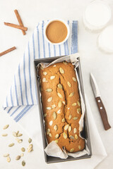Fresh homemade pumpkin bread in pan with pumpkin puree, cinnamon, nutmeg and seeds, photographed overhead.