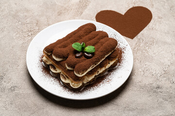 portion of Classic tiramisu dessert on ceramic plate and heart shaped cocoa powder on concrete background