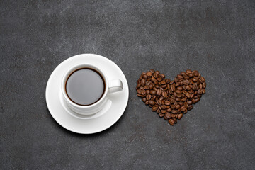 cup of fresh hot espresso coffee and heart shape made of beans on a dark concrete