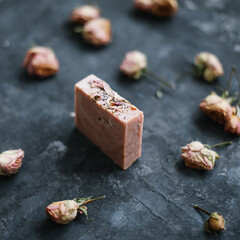 Homemade floral soap. Natural soap and rose flowers on dark background. Spa concept, body care products. Flat lay, top view