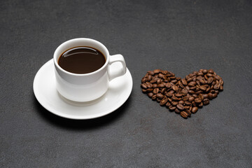 cup of fresh hot espresso coffee and heart shape made of beans on a dark concrete