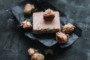 Homemade floral soap. Natural soap and rose flowers on dark background. Spa concept, body care products. Flat lay, top view