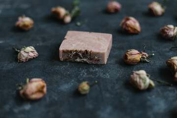 Homemade floral soap. Natural soap and rose flowers on dark background. Spa concept, body care products. Flat lay, top view