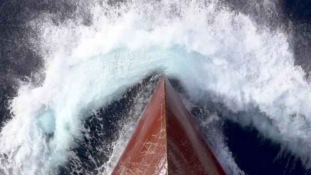 Red scratched bow of a cargo ship breaking the waves.