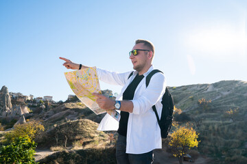Male tourist navigating with map and pointing to mountain location