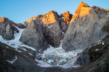 pics de montagne illuminés en jaune par le lever du soleil et glacier au dessous 