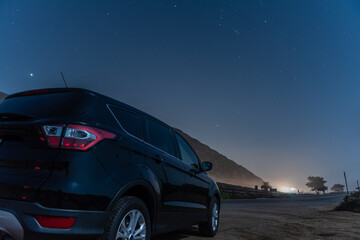 Naklejka premium Black compact car parked along highway as constellation Orion is overhead in the star lit night sky.