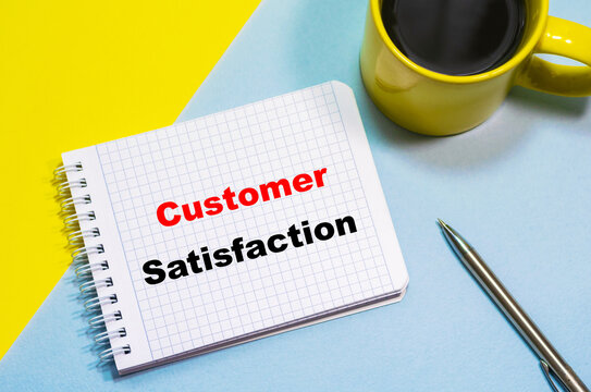Customer Satisfaction on a notepad on a blue-yellow background, a cup of coffee and a pen. Business concept
