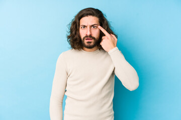 Young long hair man isolated on a blue background showing a disappointment gesture with forefinger.