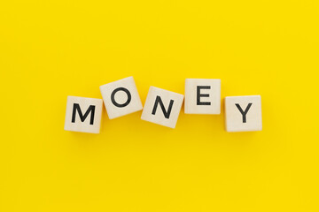 The word Money is made of wooden cubes on a yellow background.