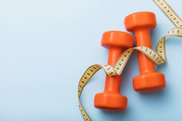 Dumbbells and measuring tape on blue background with copy space, top view