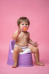 Cute baby in a diaper with a pacifier sitting on a pot. Toilet and potty training.