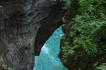 In the hollow, a blue river runs along the bottom. Mountain gorge, stone banks hang over the water of the mountain river.