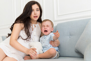 Fototapeta na wymiar sad baby crying near woman - tantrum child with mother on sofa