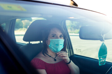 Young woman into a car wearing surgical mask and looking at camera.