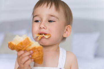happy portrait of a little smiling boy child playing and eating a croissant