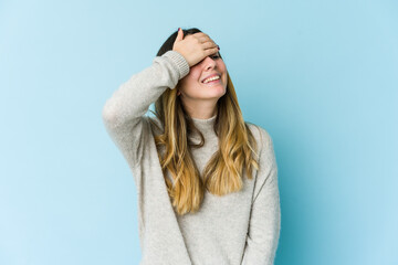 Young caucasian woman isolated on blue background laughs joyfully keeping hands on head. Happiness concept.