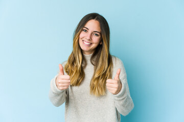 Young caucasian woman isolated on blue background smiling and raising thumb up