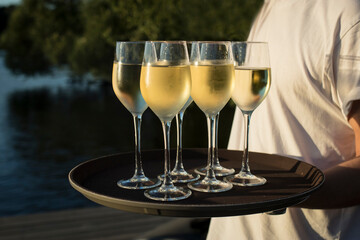 Waiter holds six glasses of champagne on tray on the beach