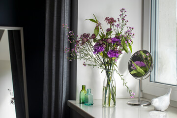 Autumn bouquet of astrantia, purple carnations and aster in a vase-bottle on the windowsill as interior decoration