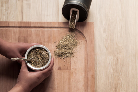 Dos manos de mujer sosteniendo un mate, fondo color madera.