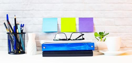 Against the backdrop of a light brick wall, stands an office table with a magnifying glass, diaries, calculator, white alarm clock, pencils and a blackboard. Workplace close-up.  Business concept