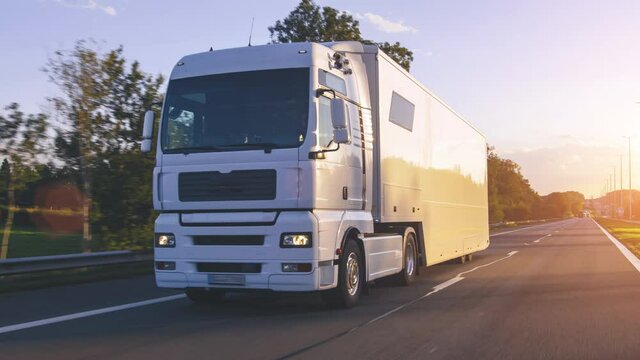 Cargo truck with cargo trailer driving on a highway. White Truck delivers goods in early hours of the Morning - very low angle drive thru close up shot.