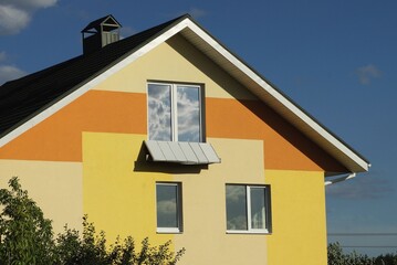 facade of a brown private house with two windows against a blue sky