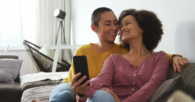Lesbian couple using mobile phone and taking picture in living room