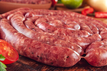 Raw thin brazilian sausages on the wooden board with ingredients - Linguiça toscaninha