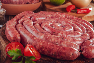 Raw thin brazilian sausages on the wooden board with ingredients - Linguiça toscaninha