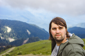 Naklejka premium Young man sit in beautiful mountains on hiking trip. Active person resting outdoors in nature. Backpacker camping outside recreation active